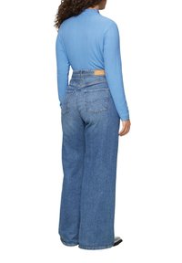 Hellblaues Langarmoberteil mit gerippter Textur, kombiniert mit hochgeschnittenen, weit geschnittenen Jeans in mittlerem Blau. Auffällige Gesäßtaschen.