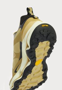 Zapatilla deportiva con parte superior amarilla y negra, paneles de malla texturada, una suela acolchada y un logo de Vibram en la suela exterior para tracción.