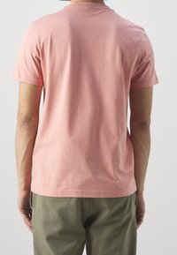 Tričko s krátkým rukávem a kulatým výstřihem v jemné růžové barvě vyrobené z měkké bavlny. Zadní strana je hladká, s rovnými lemy, kombinováno s kalhotami olivové zelené barvy.