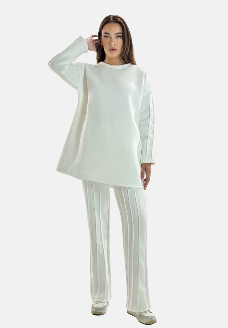 Hvid oversized sweater og matchende stribede bukser lavet af blødt stof. Sweateren har lange ærmer, mens bukserne har en flared design.