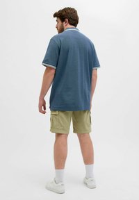 Blauwe polo met contrasterende witte kraag en sleeve strepen, gecombineerd met kaki cargo shorts en witte sneakers, bekeken van achteren.