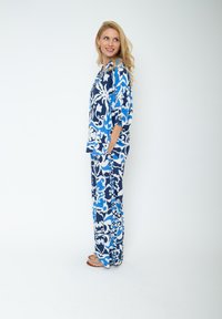 Niebieski i biały zestaw odzieży wypoczynkowej w kwiatowy wzór, zawierający luźną górę z bocznymi kieszeniami oraz pasujące spodnie w kwiatowy desen.