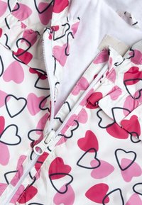 Giacca leggera con zip in base bianca, caratterizzata da un motivo a cuori colorati in rosa e rosso. Include una fodera interna bianca e chiusura con zip.