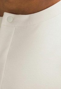 Weißer Blusenstoff mit einer glatten Textur und rundem Ausschnitt. Verfügt über einen dekorativen Knopf in der Nähe des Kragens und ein dezentes Nahtdetail.