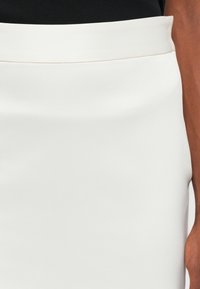 Bijela elastična suknja u obliku olovke s glatkom teksturom i širokim pojasom. Prikaz izbliza naglašava elegantan dizajn i kroj koji pristaje.