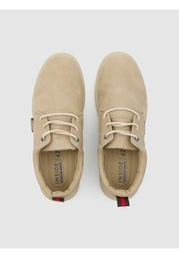 Zapatos beige con cordones, con parte superior de cuero suave, puntera redondeada y un sutil detalle del logo en el interior. Presentan una tira de agarre a contraste en el talón.