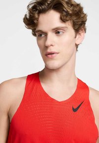 Punane sportlik kanttank, kus on võrgumuster, musta Nike logoga vasakul rinnal ja laiad õlapaelad.