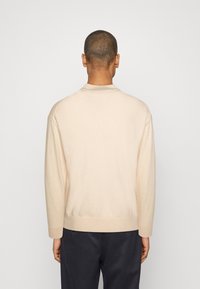 Suéter de color beige claro con mangas largas, cuello redondo y ribete acanalado, hecho de material suave, ajustado en la cintura, con textura lisa.