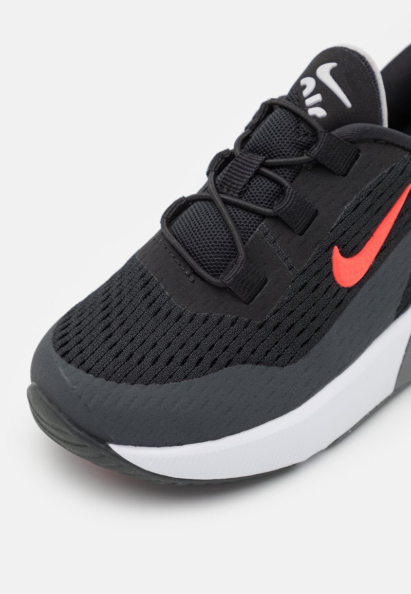 Scarpa sportiva nera realizzata in rete e materiali sintetici, con una parte superiore testurizzata, stringhe nere e un logo swoosh rosso brillante.