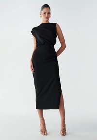 Abito midi nero con corpetto aderente, maniche corte e spacco laterale. Realizzato in tessuto testurizzato, con vita arricciata per definire la forma.