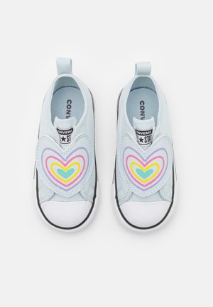 Light blue canvas slip-on shoes featuring a large multicolored heart design on the vamp, white rubber toe cap, and black rubber sole.