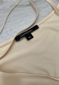 Beige top na tenké ramínka, vyrobený z hladkého materiálu. Štítek zobrazuje značku "comma" a velikost "34" na černém pozadí.