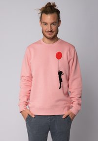 Sweatshirt en coton rose avec une silhouette noire d'un enfant tenant un ballon rouge sur le côté gauche. Encolure classique et poignets côtelés.
