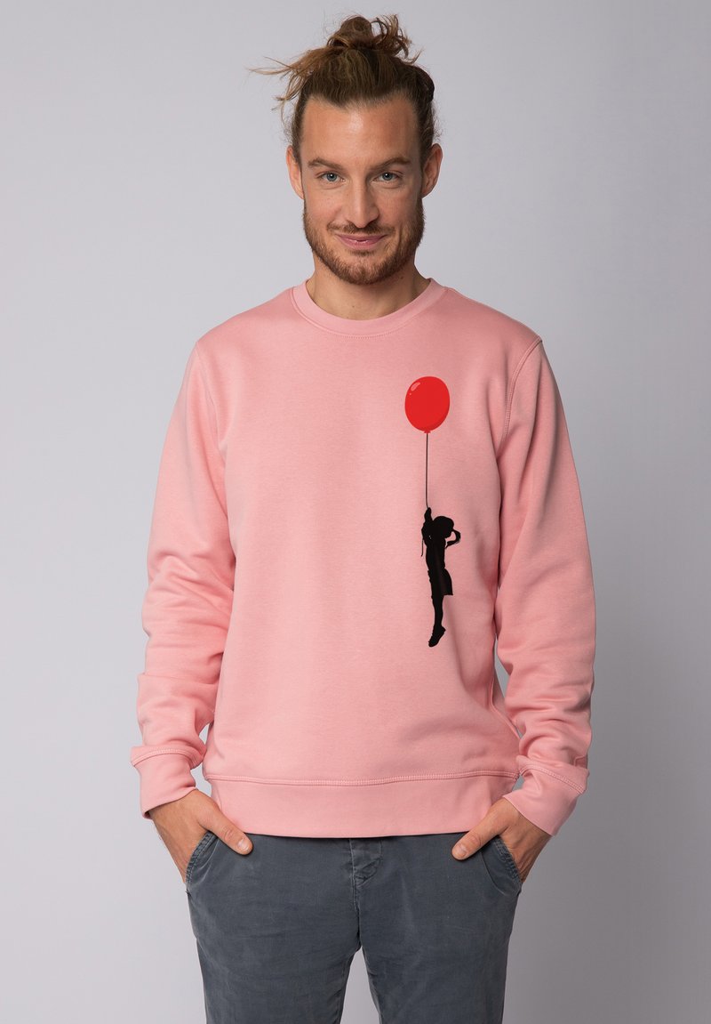 Sweatshirt en coton rose avec une silhouette noire d'un enfant tenant un ballon rouge sur le côté gauche. Encolure classique et poignets côtelés.