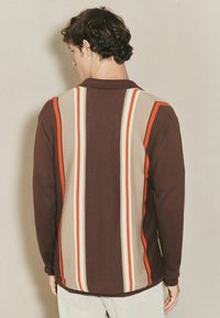 Langärmliges, braunes Poloshirt mit vertikalen Streifen in Creme und Orange. Gerippte Textur mit lockerer Passform und Kragen.