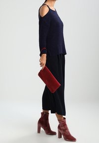 Marinblå kallaxeltröja, svarta culottes, röd mocka-clutch och burgundy klackboots med en avslappnad design och kraftiga klackar.