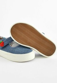 Baskets en denim à enfiler avec une semelle en caoutchouc blanc texturé, ornées d'un pompon rouge vif et d'une doublure intérieure à motifs.