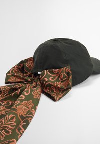 Dark green cotton cap featuring a large, patterned fabric bow in olive green and coral floral design attached at the back.