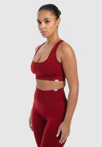 Červený sportovní crop top a legíny s vysokým pasem vyrobené z hladké a pružné látky. Obsahuje design s překříženými ramínky a jemné akcenty loga.