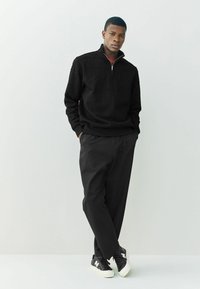 Sort lynlås sweater med tekstureret mønster, parret med løse sorte bukser og sorte sneakers med hvide accenter.