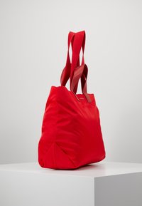 Bolsa tote roja con un aspecto acolchado, que cuenta con correas de tela anchas y un diseño minimalista. Textura suave sin patrones visibles ni herrajes.