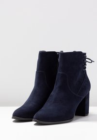 Granatowe zamszowe botki za kostkę z grubym obcasem, zamkiem błyskawicznym z boku oraz sznurowanym detalem z tyłu. Gładka tekstura i wyraźny kształt noska.