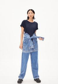Marineblauw T-shirt gecombineerd met een spijkerjack om de taille gebonden. Lossere lichtblauwe jeans en zwarte enkellaarsjes maken de outfit compleet.