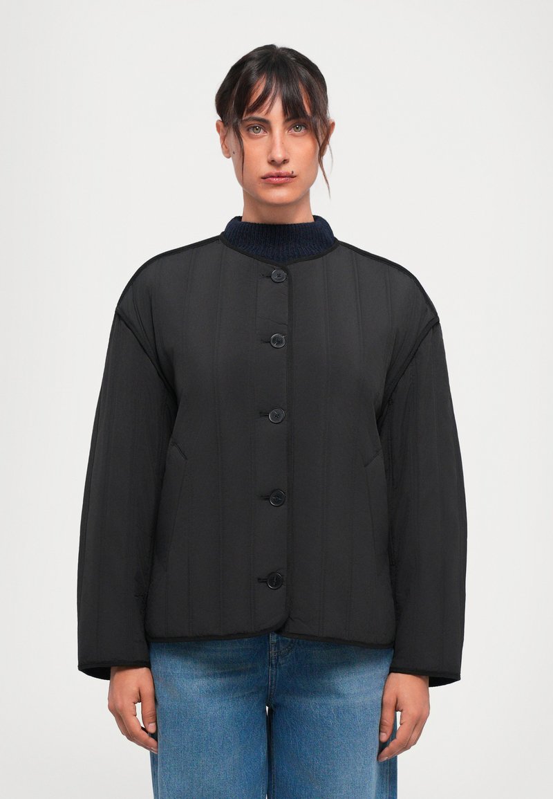 Schwarze gepolsterte Jacke mit rundem Kragen, sechs Knöpfen und zwei seitlichen Taschen. Verfügt über eine vertikale Stepptextur und einen gerippten marineblauen Kragen.