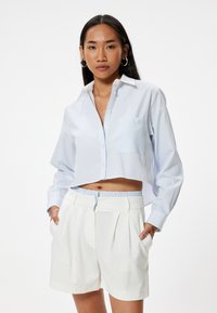 Afklippet skjorte i lyseblå med hvide striber, der har en brystlomme. Sammen med hvide plisserede shorts med elastisk talje.