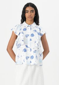 Hvit kortermet bluse med blå skjell- og sjøstjerne mønster, med knapper foran og rynkede detaljer langs skuldrene.