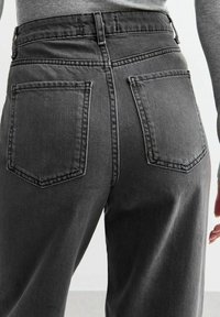 Korkeavyötäröiset, mustat farkut suoran lahkeen kanssa, joissa on kaksi takataskua ja huomaamaton ompelu. Pintakuvio näyttää hieman kuluneelta.