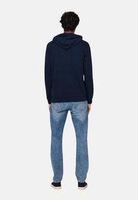 Sudadera azul marino con capucha ajustable y puños acanalados, combinada con jeans de mezclilla azul claro de corte relajado y acabado desgastado.
