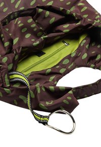 Brązowa torba materiałowa z zielonymi owalnymi wzorami, zielona wewnętrzna kieszeń z zamkiem błyskawicznym oraz czarno-biała ramiączko przymocowane do srebrnego metalowego pierścienia.
