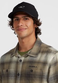 Black cap with logo, olive green shirt with plaid pattern, and a button-up closure. Features textured fabric and contrasting buttons.