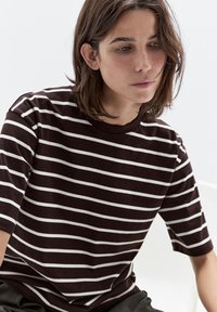 Braun-weißer gestreifter T-Shirt mit kurzen Ärmeln, einem runden Ausschnitt und einer weichen Textur. Die Streifen wechseln sich mit dicken und dünnen ab.