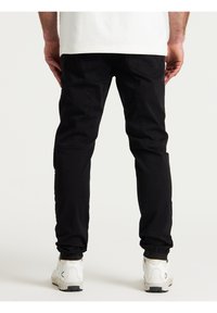 Zwarte katoenen broek met een slim fit, voorzien van achterzakken en taps toelopende enkels, gedragen met witte sneakers. Eenvoudig ontwerp, geen patronen.