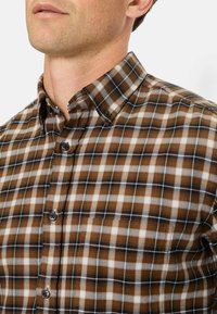 Kariertes Hemd in Braun und Weiß mit Button-Down-Kragen, das eine weiche Textur aufweist und dunkle Knöpfe an der Vorderseite hat.