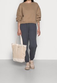 Felpa beige corta, pantaloni grigio scuro e borsa a tracolla beige con righe e manici. Sneakers grigie con dettagli chiari completano il look.