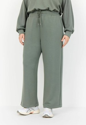 Green, wide-leg sweatpants with a drawstring waist, made from a soft fabric. Paired with white athletic shoes. Simple and functional design.
