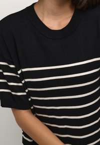 Czarna i biała koszulka w paski z ryflowanym dekoltem i krótkimi rękawami, wykonana z miękkiego materiału i w luźnym kroju.