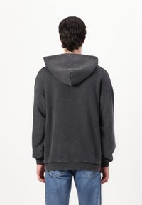 Čierny oversized mikina s veľkou kapucňou, rebrovanými manžetami a lemom. Má jemnú textúru a spadnuté ramenné švy; nosená s svetlomodrými džínsy.