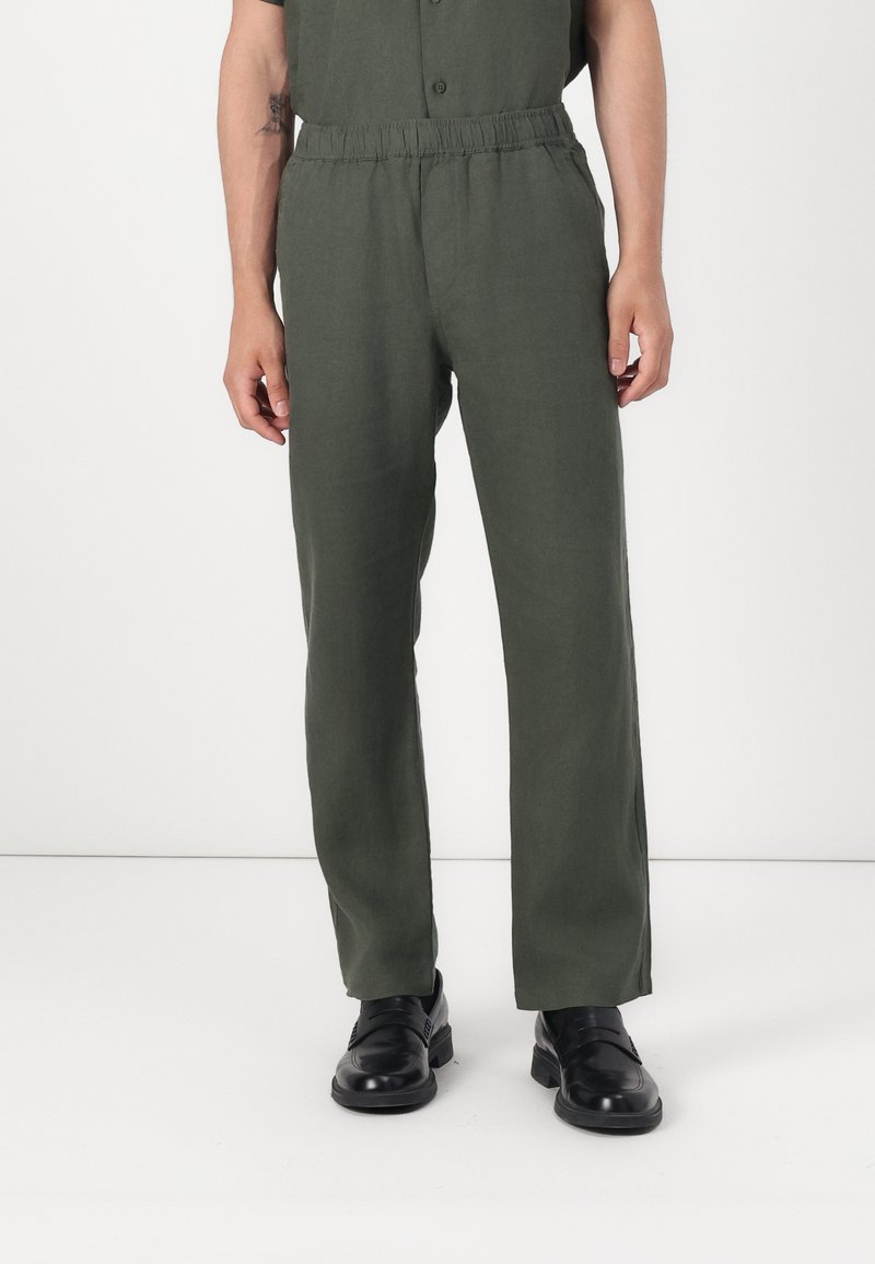 Pantaloni in lino verdi con elastico in vita, taglio dritto e due tasche laterali, abbinati a scarpe nere. Design semplice e minimalista.