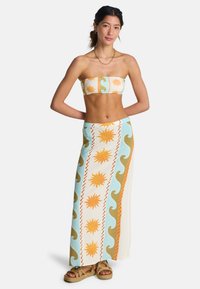 Σετ με τοπ bandeau και μακρύ φούστα σε ανοιχτό μπλε, πορτοκαλί και εκρού με σχέδια ήλιου και κυμάτων· φτιαγμένα από ελαφρύ ύφασμα.