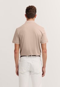 Beige polo shirt met korte mouwen, een gladde textuur en een kraag. Gecombineerd met witte broek met achterzakken. Bekijk van achteren.