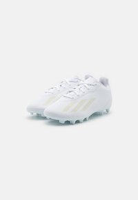 Botas de fútbol blancas con parte superior sintética suave, que cuentan con tres rayas amarillas claras, una punta redondeada y tacos de goma blanca.