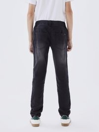 Jean en denim noir avec une coupe décontractée, une taille élastique et deux poches arrière. Le tissu présente une texture légèrement usée.