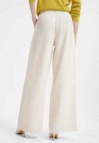 Witte wijde broek van gladde stof, met een hoge taille en centrale achterplooien. Gepaard met beige puntige hakken.