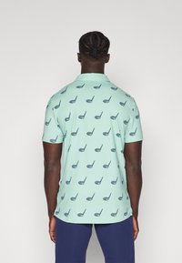 Short-sleeve polo shirt in light mint green, featuring a repeating navy blue golf club pattern, made from breathable fabric with a smooth texture.