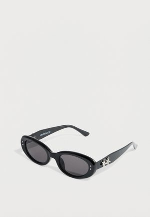 Black sunglasses with a smooth finish, oval shape, dark lenses, and silver star accent on the temples. Brand name on the arm.