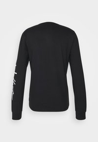 Svart långärmad T-shirt med rund halsringning, åtsittande ärmslut och ett grafiskt motiv i vitt på vänster ärm. Slät tygstruktur.